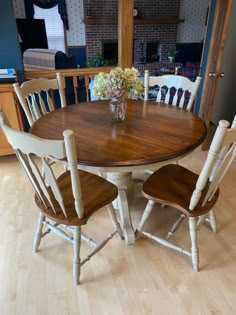 a dining room table with four chairs and a vase filled with flowers on top of it