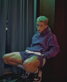 a young man sitting on top of a wooden floor next to a curtained window