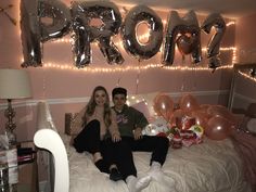 a man and woman sitting on a bed with balloons