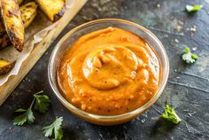 a glass bowl filled with sauce next to grilled plantains on a slate surface