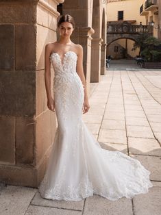 a woman standing in front of a stone wall wearing a wedding dress with an open back