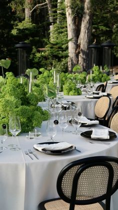 an outdoor dining area with tables and chairs set up for formal dinner in the woods