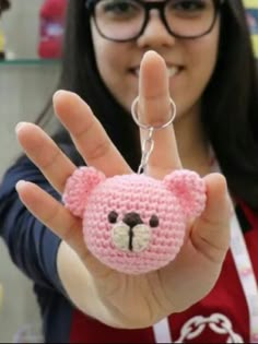 a woman is holding up a small crocheted bear keychain in front of her face