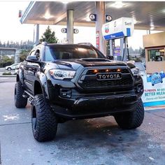 a black toyota truck is parked in front of a gas station with its lights on