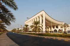 a large white building sitting on the side of a road with palm trees in front of it