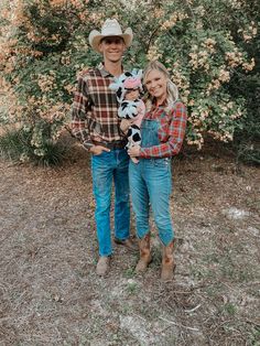 a man and woman are standing in front of some bushes holding their baby, who is wearing a cowboy hat