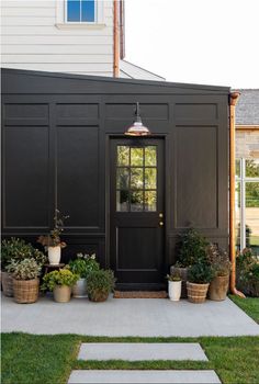 a black shed with potted plants on the front porch and side door to it