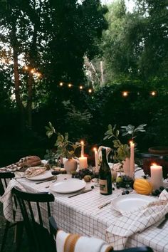 a table with plates and candles on it in the middle of a yard area surrounded by trees