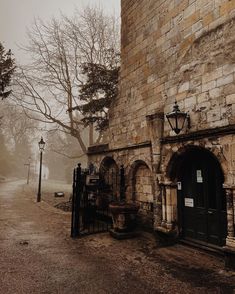 an old stone building with a gate and light post in the foreground on a foggy day