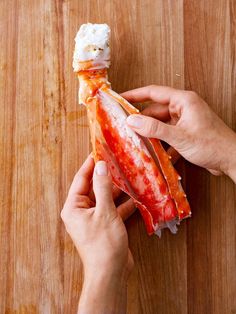 a person holding up some food on top of a wooden table next to a knife