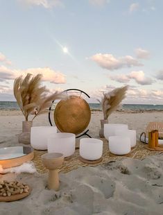 a table set up on the beach with candles, plates and vases in front of it