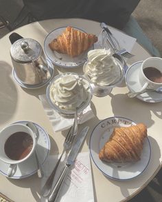 there is a croissant, cup of coffee and two cups of tea on the table