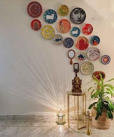 there are many plates hanging on the wall next to a potted plant and lamp