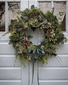 a wreath is hanging on the side of a white door with green foliage and pine cones