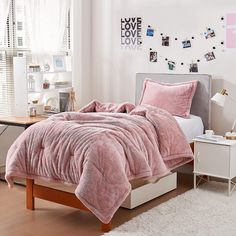 a bedroom with pink bedding and pictures on the wall above it, along with a white rug