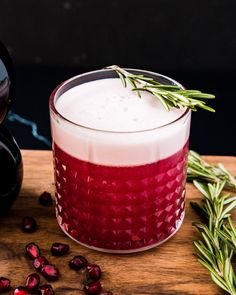 a red drink with rosemary garnish on the rim sits next to some cranberries