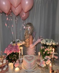 a woman standing in front of a cake with pink flowers on it and balloons behind her