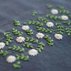 small white flowers are embroidered onto a gray cloth with green leaves and stems on it