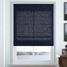 a blue roman blind in front of a window with the shades pulled back to reveal an ocean view