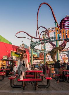 a woman sitting on top of a red picnic table in front of a carnival ride