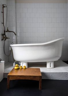 a white bath tub sitting in a bathroom next to a wooden table with rubber ducks on it