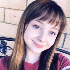 a close up of a person sitting on a bench with a brick wall in the background