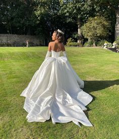 a woman in a wedding dress is standing on the grass with her back to the camera