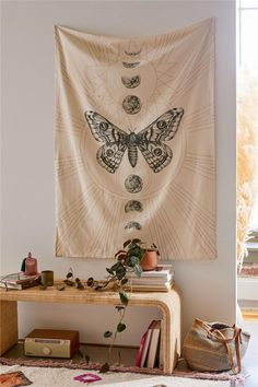 a butterfly tapestry hanging on the wall above a table with books, plants and other items