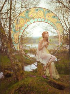 a woman in a dress sitting on top of a grass covered field next to trees