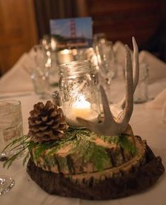 the table is set with pine cones, candles and deer antlers on top of logs