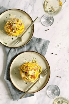 two plates with food on them sitting next to wine glasses and silverware in front of them