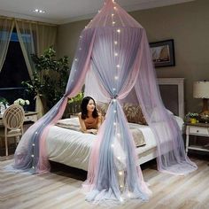 a woman laying on a bed covered in pink and blue sheer curtains with fairy lights