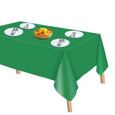 a green table cloth with white plates and silverware on it, next to a bowl of fruit