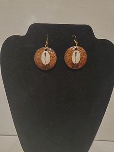 These earrings are carved out of coconut shell, stained, and adorned with Cowrie Shells. Brown Drop Earrings For Beach, Brown Drop Earrings For The Beach, Brown Earrings For Vacation, Traditional Brown Round Earrings, Unique Brown Round Earrings, Artisan Brown Jewelry For Beach, Artisan Brown Jewelry For The Beach, Artisan Brown Pierced Earrings, Traditional Brown Nickel-free Jewelry