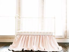 a white crib sitting in front of a window next to a wooden floor and wall