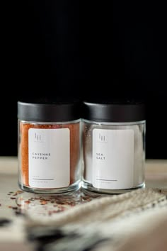 two glass jars with spices in them sitting on a table