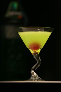 a green drink in a martini glass with a red dot on the rim and a black background