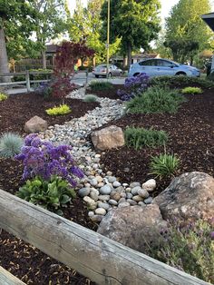 a garden with rocks and flowers in the center, along side a wooden fence that leads to a parking lot