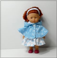 a doll with red hair wearing a blue dress and pink shoes is standing against a wall