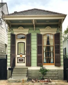 an old green house with shutters on the front and side windows, has a potted plant in front