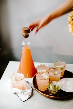 a person is pouring drinks into glasses on a table with flowers and napkins next to it