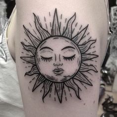 a sun tattoo with eyes closed on the side of a woman's leg,