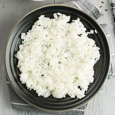 white rice in a black bowl on top of a napkin next to a fork and spoon