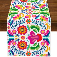 an image of a colorful table cloth on a wooden surface with flowers and leaves painted on it