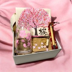 an open box with some items inside on a pink cloth covered tablecloth and in the background is a tree