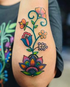 a woman's tattoo with flowers and swirls on her arm, in color