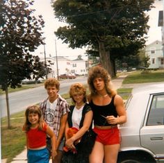 a group of young people standing next to each other near a white car on the street