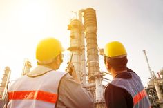 two men in hardhats standing next to an oil refinery