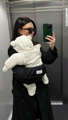 a woman taking a selfie with her cell phone while holding a baby in a sling