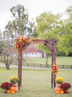 an outdoor ceremony with flowers and pumpkins on the grass in front of a wooden arch